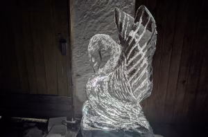 Leuchtender Schwan aus Eis mit integrierten LEDs vor Holztor – stimmungsvolle Eisskulptur für Veranstaltungen.